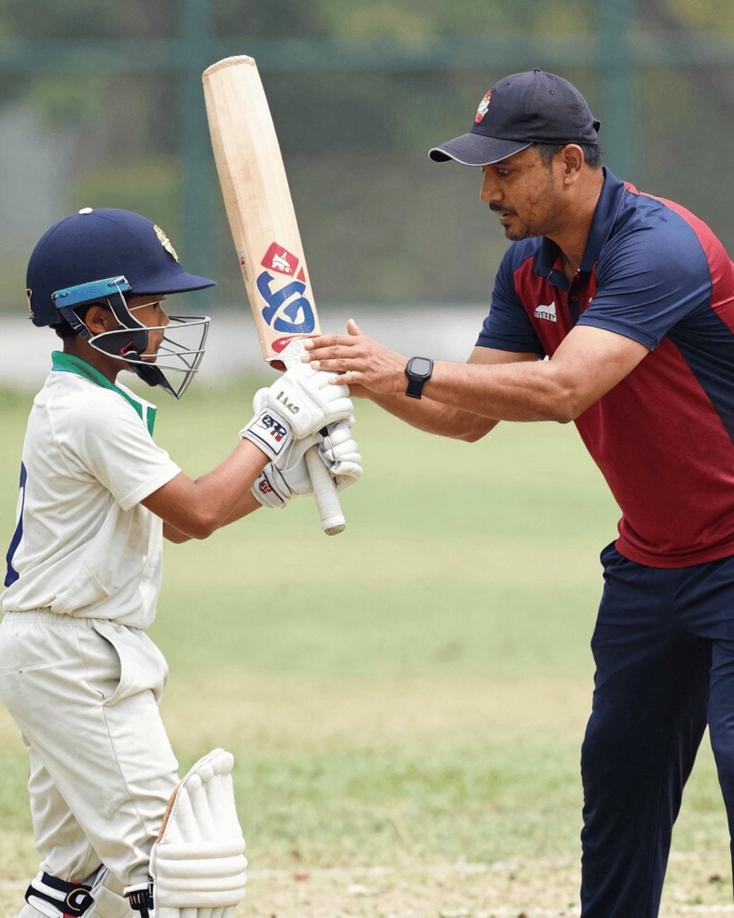 A coach guiding a young batter's grip during a practice session.